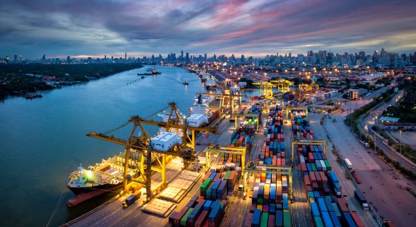 Aerial view of international port with Crane loading containers in import export business logistics with cityscape of Bangkok city Thailand at night 